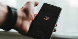 celular abrindo o aplicativo instagram, no modo escuro, com a logo num fundo preto